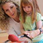 Coach showing girl how to use tennis racquet.