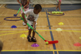 Children playing ball hockey on indoor basketball court.