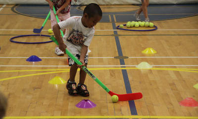 Children playing ball hockey on indoor basketball court.