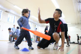 Toddler hi-fiving Sportball coach while playing indoor baseball.