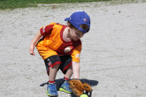 Young boy picking up tennis ball with baseball glove.