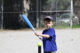 Young boy hitting tennis ball off a ball-holder with a baseball bat.