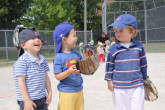 Children laughing together while playing outdoor baseball.