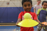 Young boy holding tennis ball and cone during Sportball multi-sport class.