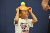 Young boy balancing ball and cone on head during Sportball multi-sport class.