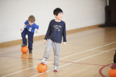 Kids balancing soccer ball under feet.