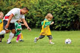 Sportball coach encouraging young boy to run across field in soccer class.